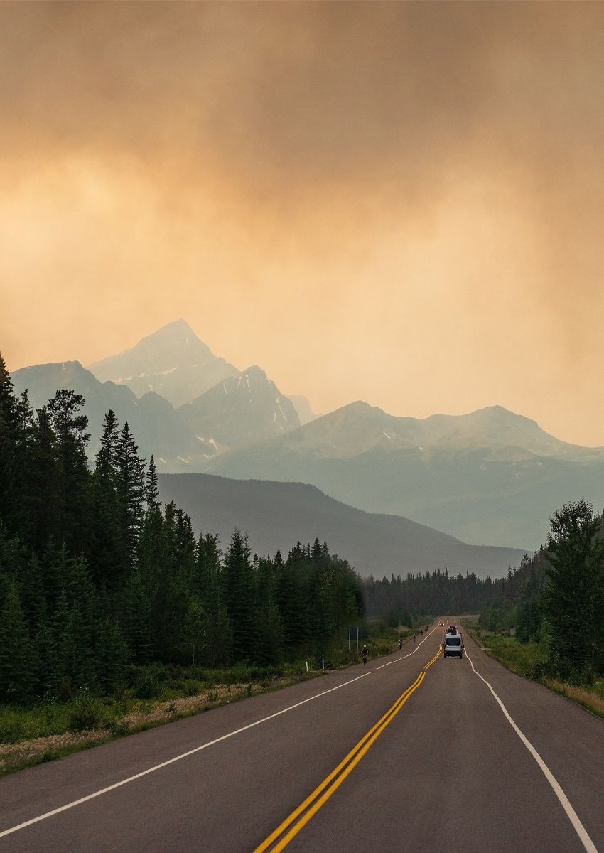 Wildfire smoke over a highway in British Columbia with forest on either side and mountains in the distance.