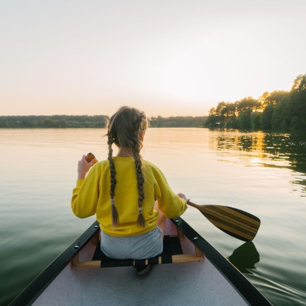 A young woman seen from behind paddling a canoe on a lake at dusk